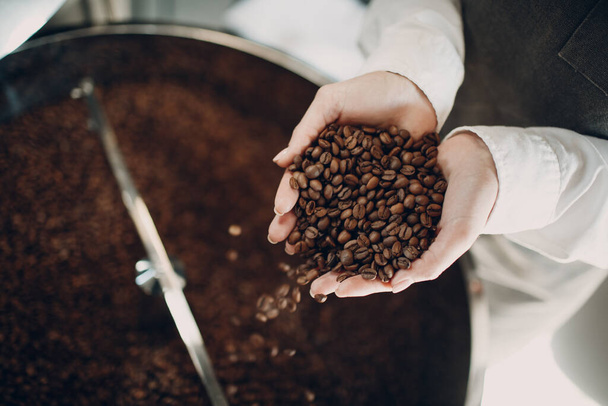 Kaffeekühlung in der Röstmaschine bei der Kaffeeröstung. Junge Arbeiterbaristin mixt Kaffeebohnen und hält sie in Händen. - Foto, Bild