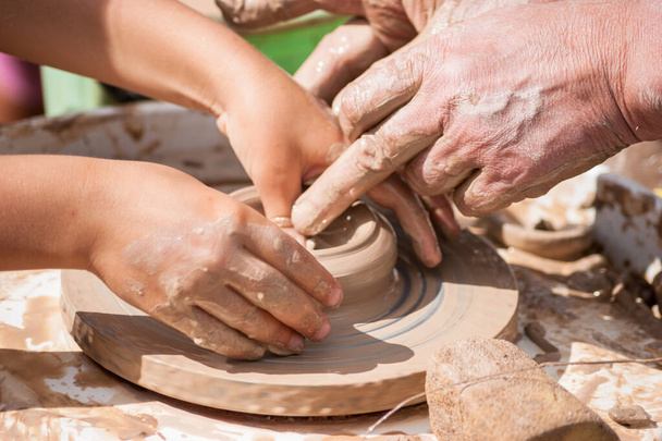 Allenamento di ceramica - mani maschili e bambini fanno una brocca di argilla sulla ruota di un vasaio, primo piano - Foto, immagini