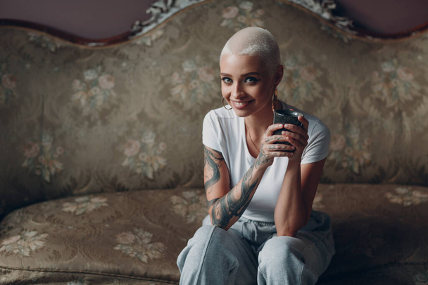 Millenial młoda kobieta z krótkimi blond włosy portret siedzi na kanapie vintage. - Zdjęcie, obraz