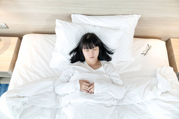 Asiática mujer duerme en la cama blanca después de agotado y probado todo el día. - Foto, Imagen