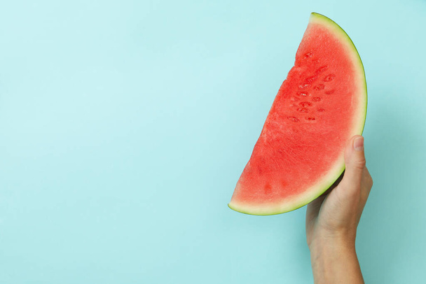 Female hand holds watermelon slice on blue background - Fotoğraf, Görsel