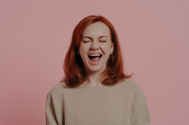 Overjoyed red-haired woman laughing positively, with closed eyes, isolated on pink background - Photo, Image