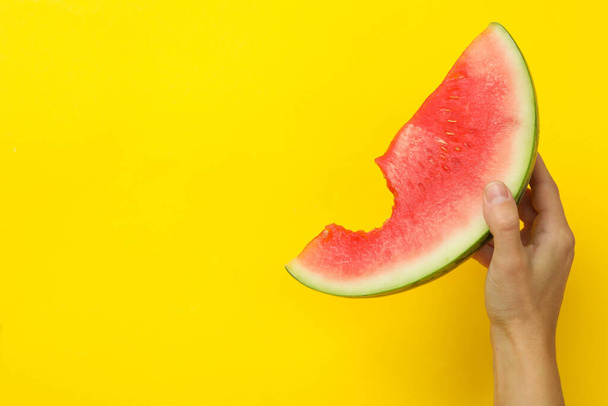 Vrouwelijke hand houdt watermeloen slice op gele achtergrond - Foto, afbeelding