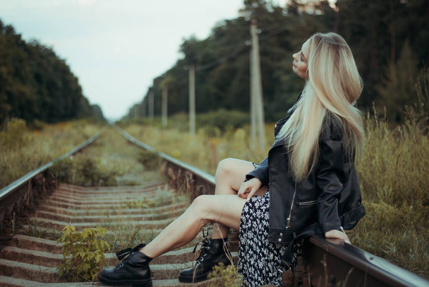 Young beautiful girl in black clothes, on the railroad tracks. Beautiful blonde in a good mood. Beautiful natural soft evening light - Foto, Imagem