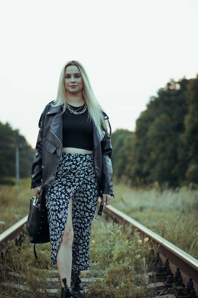 Young beautiful girl in black clothes, on the railroad tracks. Beautiful blonde in a good mood. Beautiful natural soft evening light - Zdjęcie, obraz