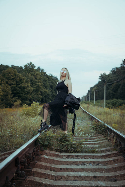Young beautiful girl in black clothes, on the railroad tracks. Beautiful blonde in a good mood. Beautiful natural soft evening light - Foto, imagen