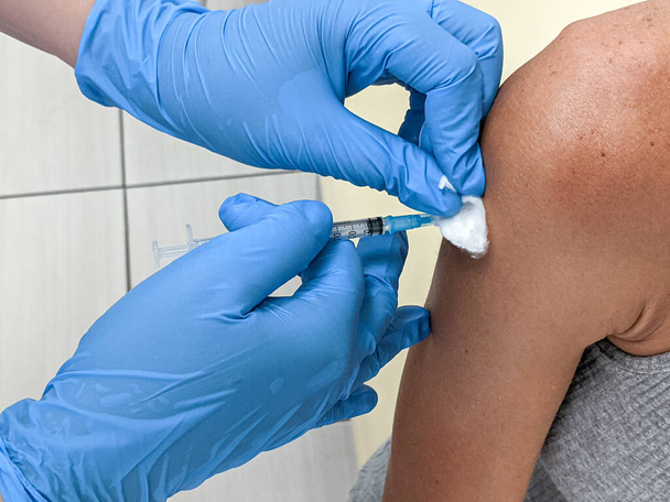 Close up of adult woman  getting covid vaccine in clinic or hospital, with nurse injecting vaccine into shoulder - Valokuva, kuva