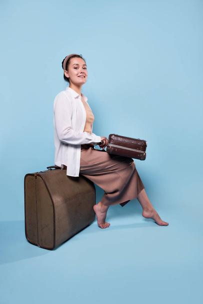 happy young woman in summer pants and a white shirt is sitting on suitcases - Foto, Imagem