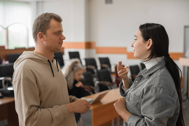 The girl and the guy talk in sign language. Two deaf students chatting in a university class. - Фото, изображение
