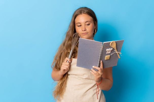 Молодая девушка держит и позирует с кухонной утварью на синем фоне - Фото, изображение