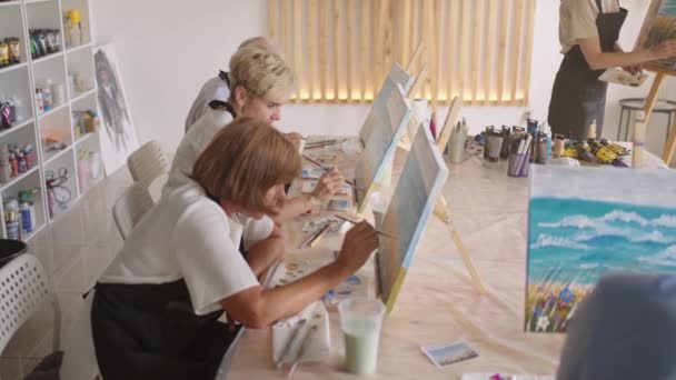Una anciana jubilada pinta un cuadro junto con sus amigos. Un grupo de viejos amigos y una mujer mayor están dibujando juntos. - Metraje, vídeo