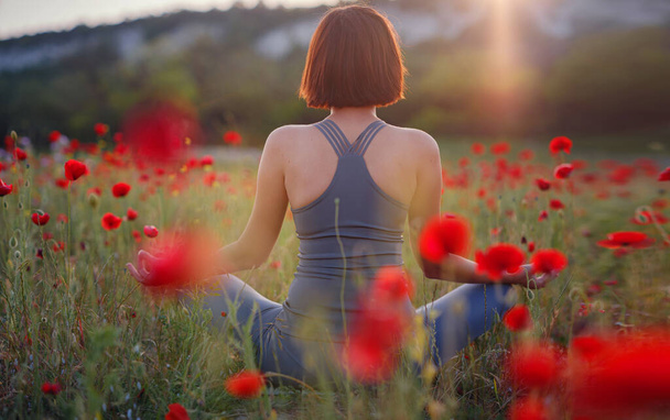 Una hermosa mujer medita en un campo de amapola al atardecer - Foto, Imagen