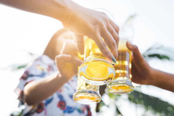 Tiro cortado de pessoas segurando copos de cerveja comemorando na festa de acampamento de verão ao ar livre. Amigos clinking garrafa de cerveja durante o acampamento ao ar livre - Foto, Imagem