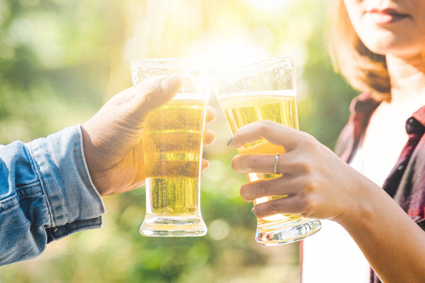Vystřižený záběr lidí držících sklenice na pivo, jak slaví v letním táboření venku. Přátelé cinkání láhev piva během kempování venku - Fotografie, Obrázek