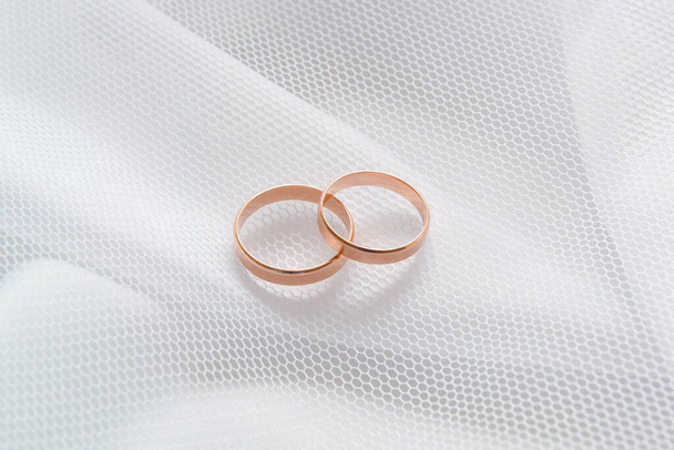Gold wedding rings on white cloth under a white mesh veil. Close-up. - Foto, imagen