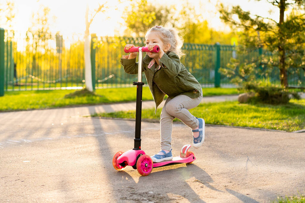 Little blonde girl on a scooter near school - Foto, Imagen