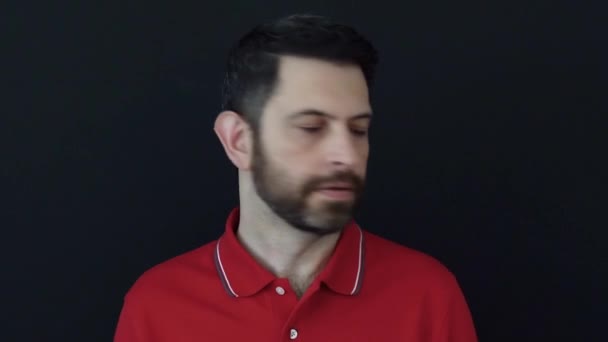 Deluso e scontento uomo di 30 anni indossa una t-shirt rossa posa isolato su sfondo nero in studio. Concetto di emozioni scontente e frustrate. - Filmati, video