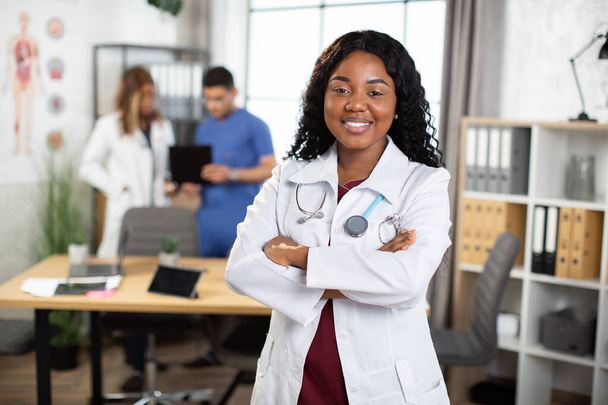 Afro-American doctor posing with arms crossed and diverse medical team working on the background - 写真・画像