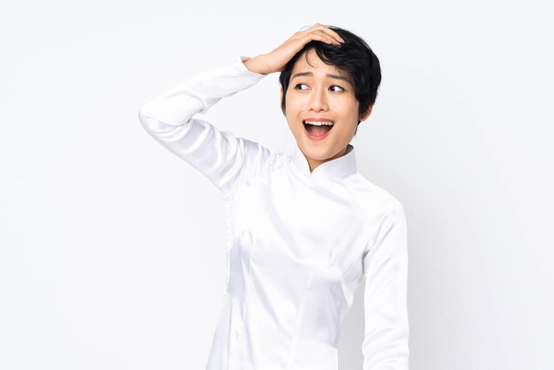 Young Vietnamese woman with short hair wearing a traditional dress over isolated white background doing surprise gesture while looking to the side - Photo, image