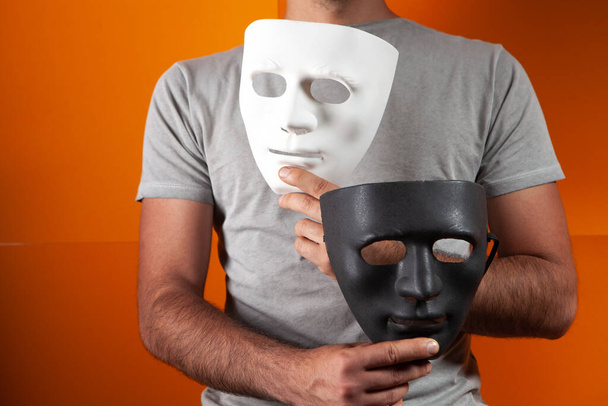 een man met een wit en zwart anoniem masker op een oranje achtergrond - Foto, afbeelding