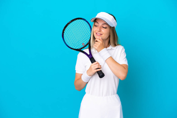 Young tennis player Romanian woman isolated on blue background looking to the side and smiling - Photo, Image