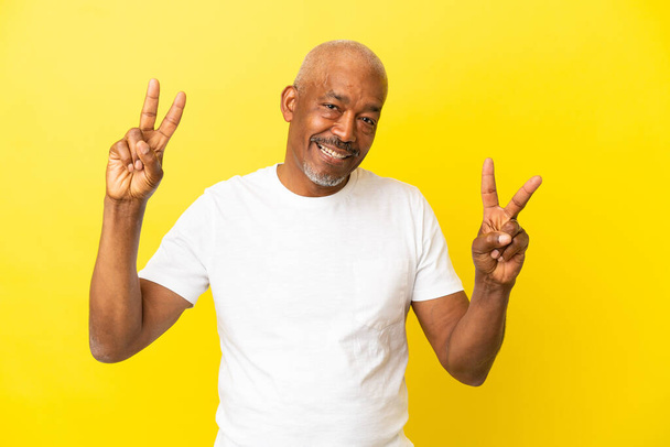 Kubanischer Senior auf gelbem Hintergrund isoliert und zeigt mit beiden Händen das Siegeszeichen - Foto, Bild