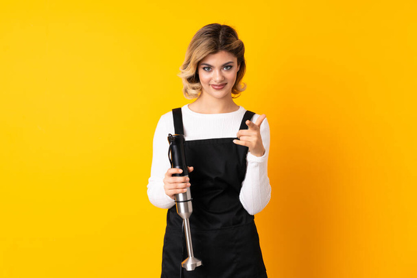 Girl using hand blender isolated on yellow background surprised and pointing front - Photo, Image