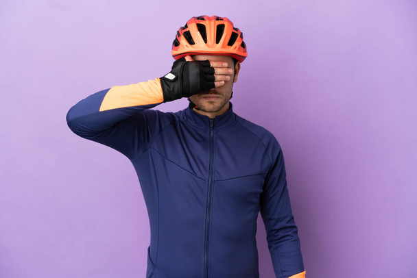 紫色の背景に手で目を覆う若いブラジル人サイクリストの男性。何か見たくない - 写真・画像