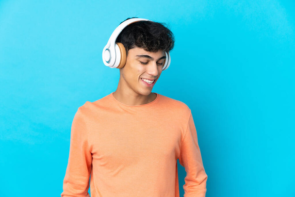 Молодий чоловік над ізольованим синім фоном прослуховування музики
 - Фото, зображення