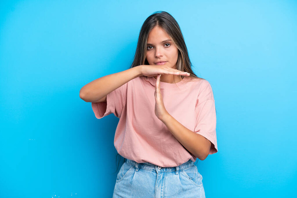 Young caucasian woman isolated on blue background making time out gesture - Foto, afbeelding