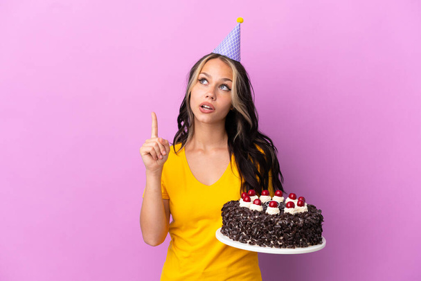 Adolescente rusa chica sosteniendo pastel de cumpleaños aislado sobre fondo púrpura pensando en una idea apuntando con el dedo hacia arriba - Foto, imagen