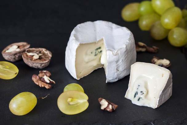 Brie-tyyppinen juusto. Pehmeä juusto rypäleiden ja saksanpähkinöiden kanssa mustalla pohjalla - Valokuva, kuva