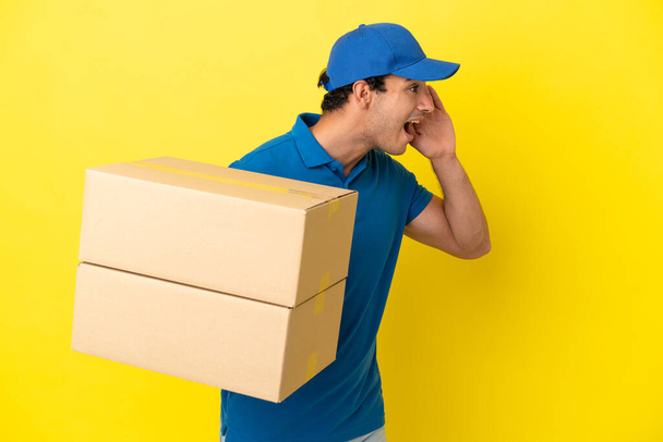 Delivery man over isolated yellow wall shouting with mouth wide open to the side - Foto, Bild