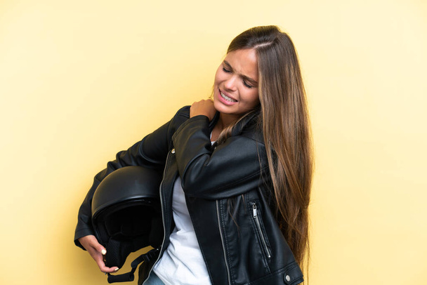 Mladá běloška žena s motocyklovou přilbou izolované na žlutém pozadí trpí bolestí v rameni za to, že vynaložil úsilí - Fotografie, Obrázek