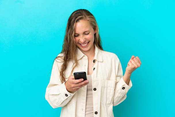 Young caucasian woman isolated on blue background surprised and sending a message - Photo, Image