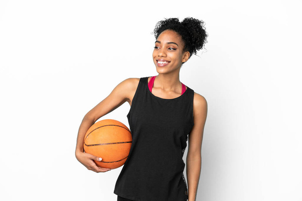 Genç basketbolcu Latin kadın, beyaz arka planda izole edilmiş, yan tarafa bakıyor ve gülümsüyor. - Fotoğraf, Görsel