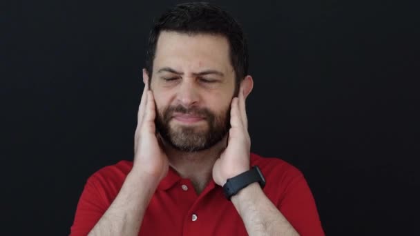 Hombre cubriéndose las orejas debido a la inquietud del ruido, vistiendo una camiseta roja aislada sobre fondo negro. Molesto por demasiado ruido, filmado en el estudio. - Imágenes, Vídeo