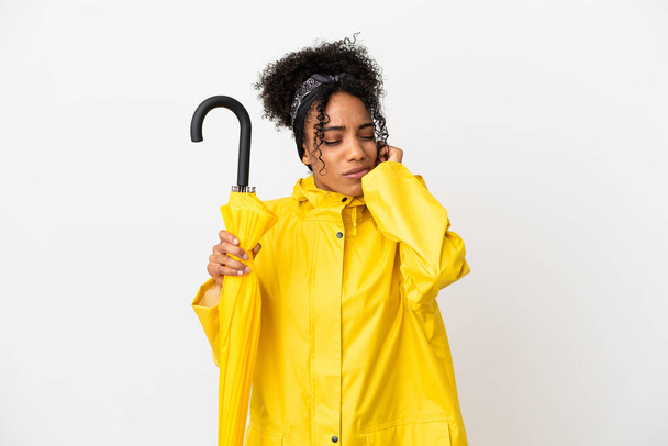 Mujer joven con capa impermeable y paraguas aislado sobre fondo blanco frustrado y cubriendo las orejas - Foto, Imagen