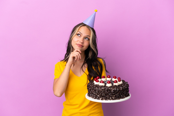 Adolescente russe fille tenant gâteau d'anniversaire isolé sur fond violet et regardant vers le haut - Photo, image