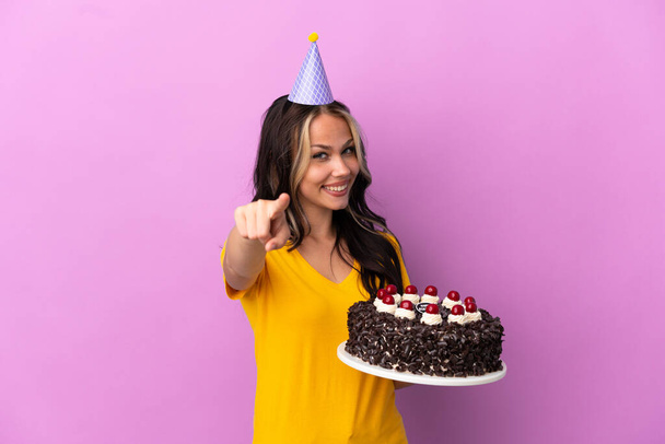 Teenager Russian girl holding birthday cake isolated on purple background pointing front with happy expression - Photo, image