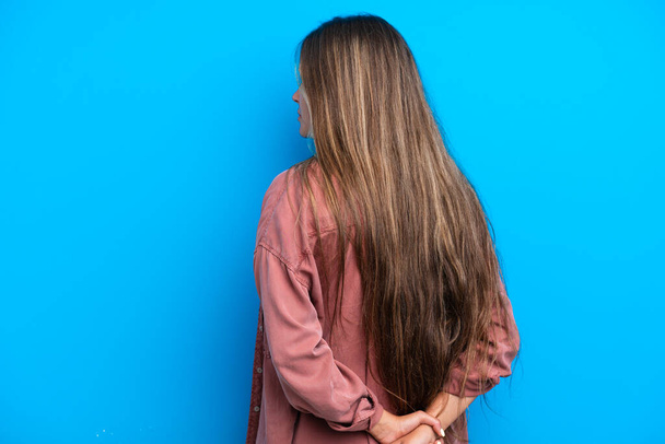 Young caucasian woman isolated on blue background in back position and looking back - Photo, image