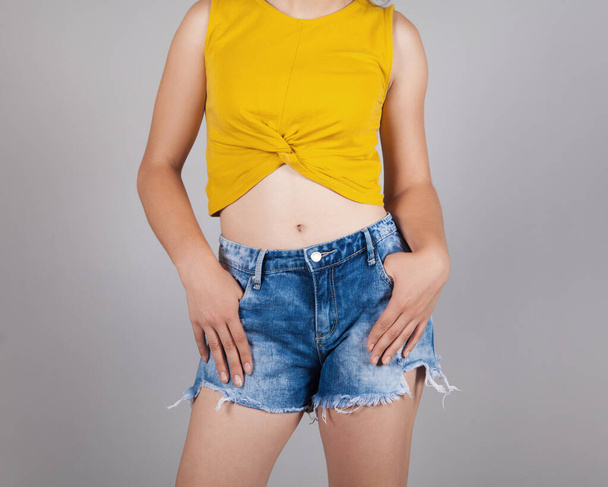 Caucasian young woman in jeans shorts, on gray background. - 写真・画像