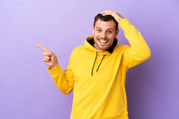 Brazilian man over isolated purple background surprised and pointing finger to the side - Foto, imagen