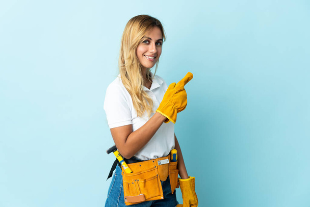 Mladá blondýnka Uruguayský elektrikář žena izolované na modrém pozadí ukazuje na stranu prezentovat produkt - Fotografie, Obrázek