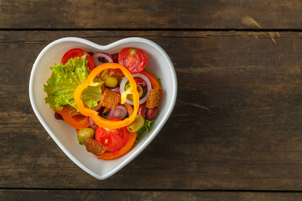 Vegetable salad in a heart shape plate on a wooden table. Horizontal photo - Fotoğraf, Görsel