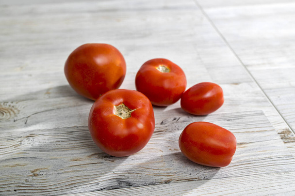 Different types of fresh tomatoes lie on a beige wooden table - Photo, image