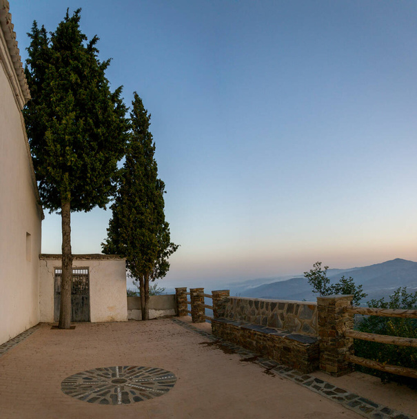 Вид на церкву Юбар в Алпуджаррі з кам'яними лавками, огорожею і двома соснами на задньому плані під час заходу сонця. - Фото, зображення