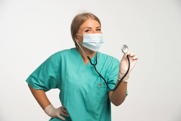 Doctora rubia usando mascarilla facial y comprobando con estetoscopio. Foto de alta calidad - Foto, Imagen