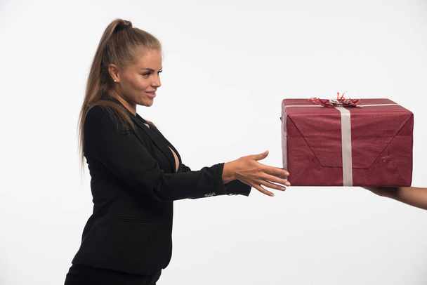 Młoda bizneswoman w czarnym garniturze otrzymuje duże pudełko z prezentami. Wysokiej jakości zdjęcie - Zdjęcie, obraz