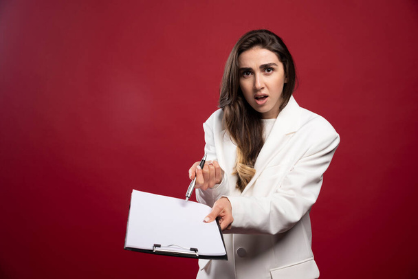 Geschäftsfrau mit aufgeschlagenem Notizbuch auf rotem Hintergrund. Hochwertiges Foto - Foto, Bild